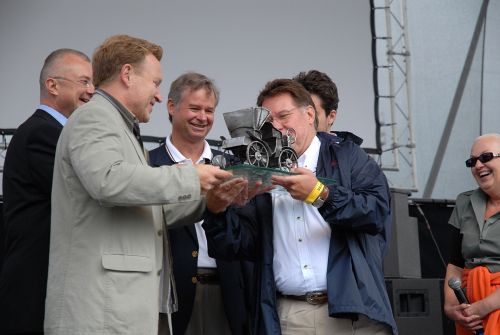 Šéf Tatry Ronald Adams přebírá dárek od starosty města. Předání modelu prvního vozu  přihlížel také velvyslanec Spojených států amerických Richard Graber (uprostřed).